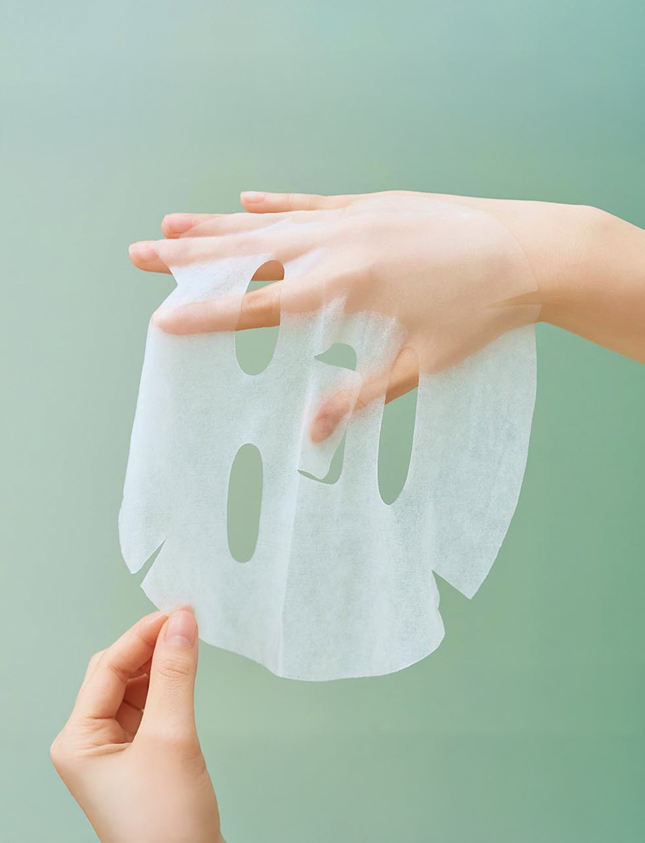 Transparente, dünne Sheet-Maske wird über eine Hand gehalten, um die leichte und flexible Textur zu zeigen.