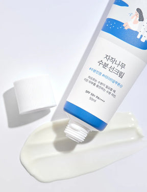 Der Deckel der Birch Moisturizing Sunscreen ist abgeschraubt und das Produkt liegt auf einem Swatch der Textur.
