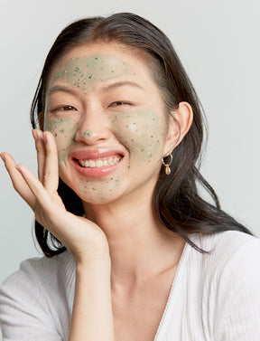 Eine Frau trägt das AXIS-Y Mugwort Pore Clarifying Wash Off Pack auf ihr Gesicht auf.